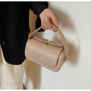 Close-up of beige leather handbag featuring a gold shell clasp and fashion typography