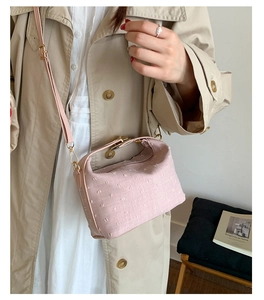 Detail of macaron pink textured crossbody bag worn with a stylish beige trench coat.