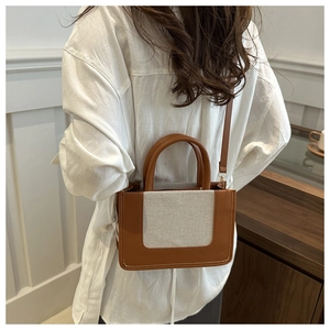 Detail of a brown leather and beige canvas patchwork tote bag with rounded handles