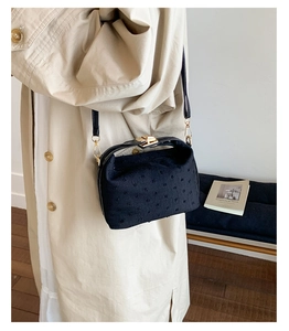 Detail view of an elegant black textured crossbody bag paired with a stylish beige trench coat