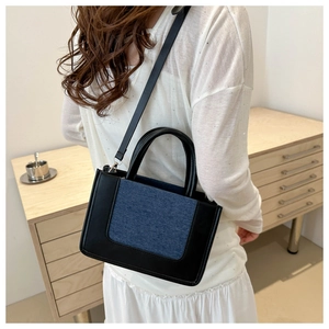 Detail of trendy color-block crossbody bag featuring blue denim and black leather contrast