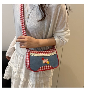 Detailed view of blue denim crossbody bag featuring red gingham trim and cherry patch