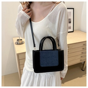 Classic black and blue denim patchwork satchel bag shown styled on a model in a minimal room