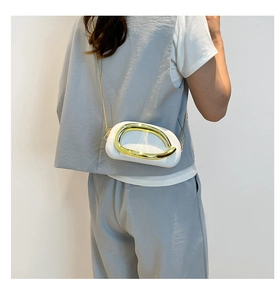 Detail of white semicircular crossbody bag with gold metal trim on model's grey outfit