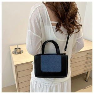 Detail of contrast patchwork handbag featuring black leather and blue denim material
