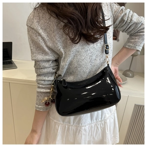 Detail of glossy black patent leather shoulder bag with cherry charm accessory