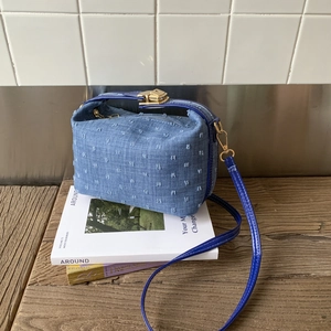 Detail shot of a trendy blue denim crossbody bag with textured puff ball accents