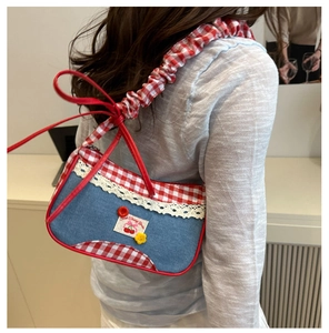 Detail of denim shoulder bag with red plaid trim, lace edges, and cherry patch