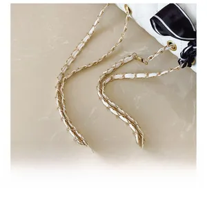 Detail of white quilted leather bag with gold chain strap and decorative silk scarf knot