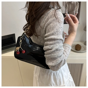 Detail of glossy black patent leather baguette bag with gold chain and cherry charm