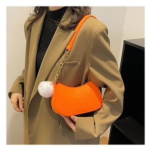 Detail view of a vibrant orange quilted shoulder bag featuring a white pom-pom charm