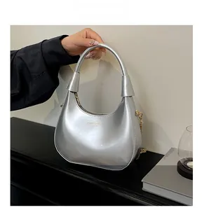 Detail view of silver crescent bag featuring reflective patent leather and gold chain strap