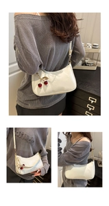 Detailed view of white patent leather shoulder bag with cherry pendant and gold hardware