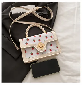 Close-up detail of a cream crossbody bag featuring a strawberry print and flower lock