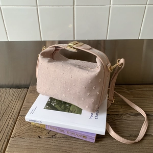 Elegant macaron pink textured crossbody bag styled on aesthetic books in a modern interior