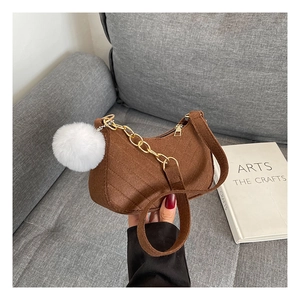 Detail view of brown quilted shoulder bag with white pompom charm on a grey sofa