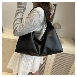 Close-up of minimalist black hobo bag with cracked leather texture and wide strap