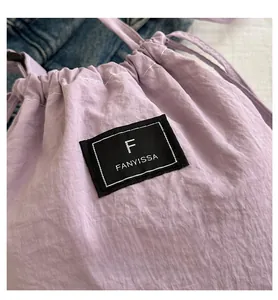 Detail of light purple drawstring nylon bag featuring a black woven brand label