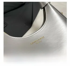 Close-up of silver crescent bag featuring brushed metallic texture and gold logo detail