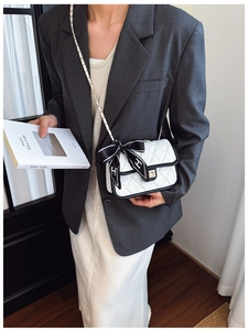Close-up of a white quilted shoulder bag featuring a contrast bow and golden chain strap