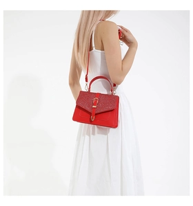 Détail du sac rouge en cuir avec rabat pailleté et boucle métallique dorée en forme de V