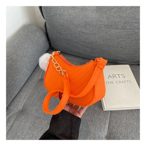 Detailed view of an orange felt shoulder bag with a stylish white pom-pom charm