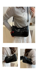 Detail of black patent leather underarm bag with red cherry charm and chain decor