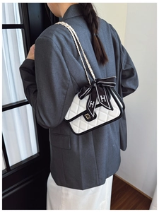 Close-up of quilted leather bag with contrast bow, metal chain, and gold buckle on a model