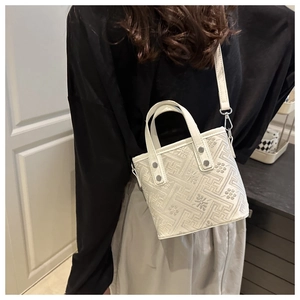 Close-up of geometric floral embroidery and silver rivets on a cream bucket bag