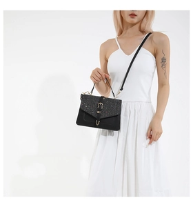 Detail view of black crossbody bag with shimmering flap and golden metallic hardware