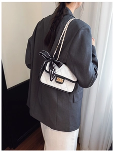 Detail of white quilted shoulder bag with black trim and elegant H-logo silk ribbon accessory