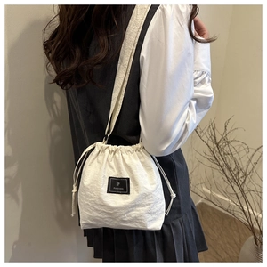 Detail view of a white drawstring bucket bag with a minimalist black woven logo patch