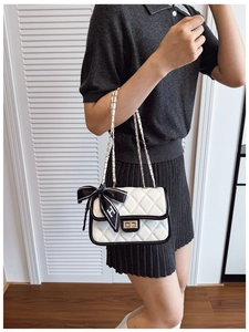 Detail of quilted shoulder bag with chain strap and decorative silk ribbon bow