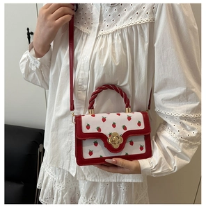 Close-up detail of a chic red and white strawberry print handbag held by a model