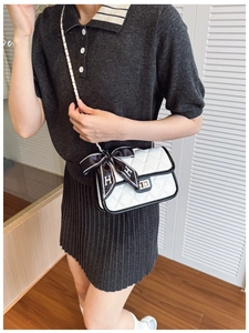 Close-up of quilted white crossbody bag with black trim and silk scarf detail