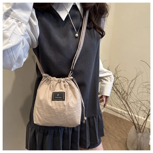 Detailed macro view of beige pleated fabric bucket bag with F FANYISSA brand label