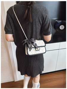 Close-up of quilted white shoulder bag with black trim, silk bow, and gold hardware