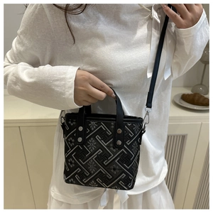 Detail of a black crossbody bag with silver geometric embroidery and metal rivets