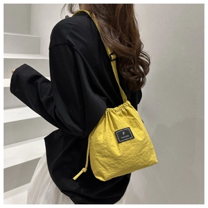 Detail view of yellow drawstring crossbody bag with brand logo patch on light nylon fabric