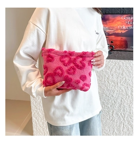 Close-up of a vibrant pink plush cosmetic pouch with cute heart patterns held by a model