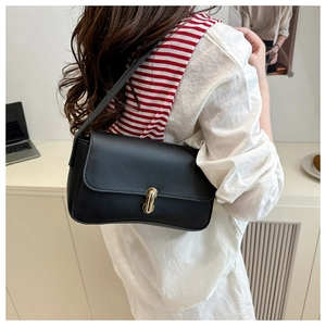 Close-up of black leather baguette bag with oval gold buckle worn by a model