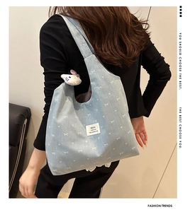 Close-up of light blue canvas tote bag with bow pattern and plush charm on shoulder