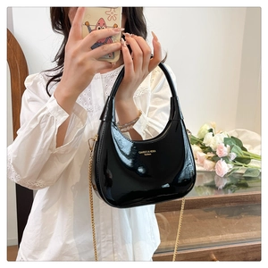 Detail of glossy black hobo bag with a golden chain strap and smooth patent leather finish