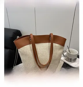 Detail shot of the woven straw tote bag featuring brown leather handles and stitching