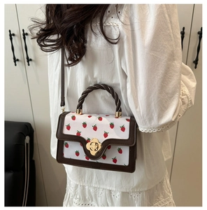 Detailed view of a strawberry print handbag with a brown trim and twisted handle