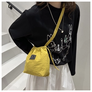 Detail of yellow nylon drawstring bucket bag with black square logo label