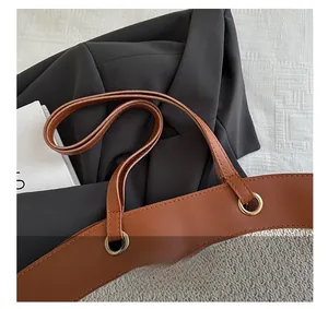 Detail of straw woven tote bag featuring brown leather handle and gold metal eyelets