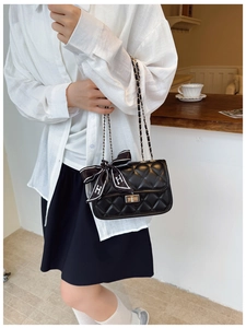 Detail of black quilted leather shoulder bag with gold chain strap and H silk scarf bow