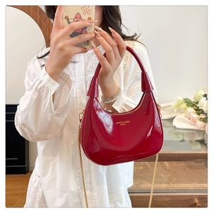 Detail of red patent leather crescent bag with gold chain strap and brand logo