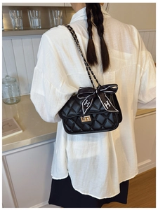 Detail of black quilted chain bag with gold metal clasp and H-pattern silk ribbon